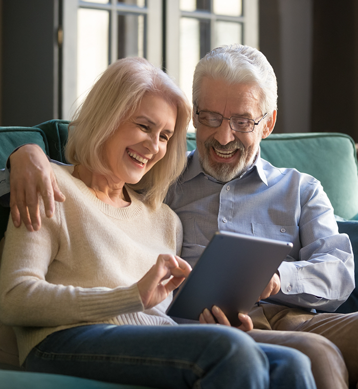 Senior man and woman sitting on couch and looking at tablet