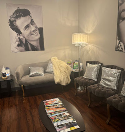 The image shows an interior space with a large poster of a man on the wall, a couch, chairs, a coffee table, and various items such as books, magazines, pillows, and a blanket.