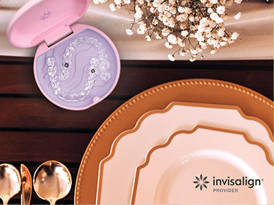 The image displays a collection of tableware items, including plates, a serving tray, and a decorative box with an intricate design, all arranged on a wooden surface with a floral centerpiece, suggesting a setting for a formal meal or event.