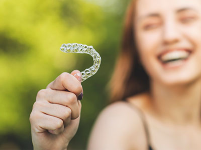 An individual is holding up a clear plastic dental retainer with a smile, possibly indicating dental health or orthodontic appliance.