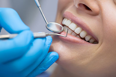 An image shows a person receiving dental care with a toothbrush being used on their teeth by a dental professional wearing blue gloves, with the focus on the dental work being performed.