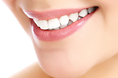 The image features a close-up view of a person s face with a focus on their teeth, which are being showcased by a smile, against a white background.