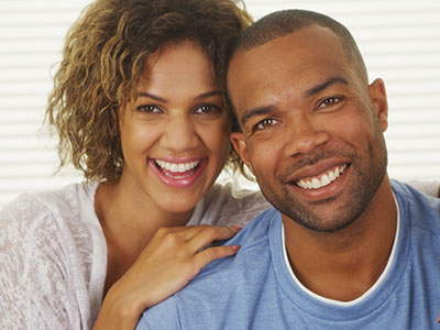 A man and woman smiling together, with the woman standing behind the man.