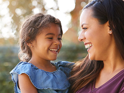 A woman and child are smiling at each other outdoors.