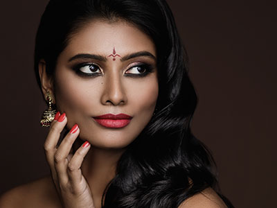 The image features a woman with dark hair and makeup, posing with her hand on her chin against a neutral background.