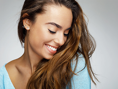 A young woman with long hair smiles directly at the camera against a plain background.