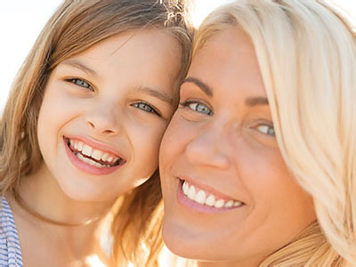 A woman and a young girl smiling at the camera, with the woman s arm around the child s shoulders.