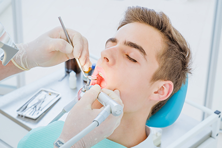 A young man receiving dental treatment with a dentist using specialized equipment.