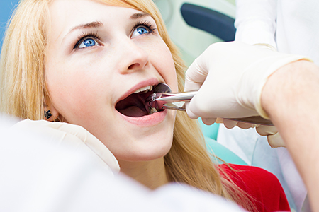 A woman receiving dental care from a dentist, with her mouth open and the dentist adjusting her teeth.