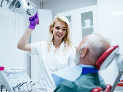 A woman dentist assisting an older man with dental treatment.