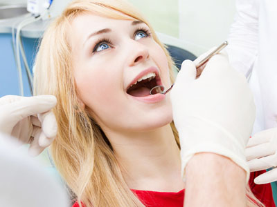 A woman receiving dental care, seated in a dental chair with her mouth open, while a dentist works on her teeth using a drill.