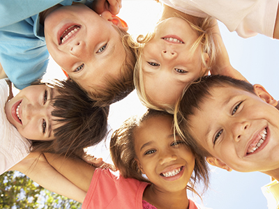 A group of children posing for a photo with smiles on their faces, against a clear sky background.