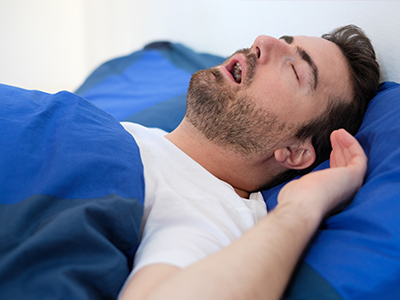 A man sleeping peacefully on his back in bed with blue sheets.