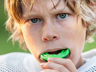 The image displays a young male athlete holding a green mouthguard, with a serious expression looking directly at the camera.