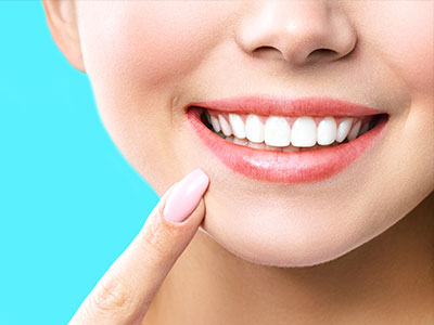 The image shows a close-up of a smiling woman with her eyes closed, looking upwards towards her nose. She has light skin, neatly manicured nails, and is wearing lipstick.